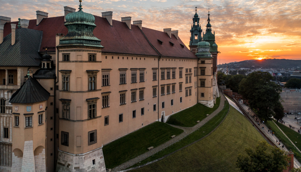 widok na fragment zamku wawelskiego, na skrajach budynku wieże, w tle krajobraz i zachód słońca