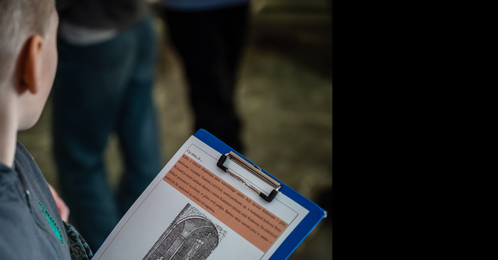 Dziecko uczestniczące w zajęciach w muzeum, w ręce trzyma kartę zadań do wypełnienia.