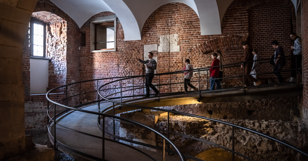 Osoby oglądające wnętrza w muzeum, z zainteresowaniem podziwiające szczegóły wystawy i wypełniające karty zadań.