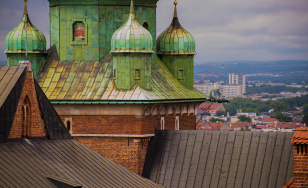 fragment zamkowego dachu z blachy, ceglane ściany i metalowy dach wieży, w tle zabudowa miasta i wzgórza na horyzoncie
