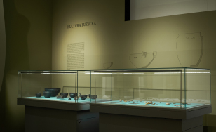 sala wystawy, na ścianie tekst opisowy, w szklanych gablotach obiekty archeologiczne, nastrojowe światło