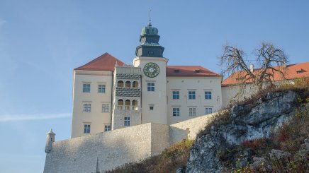 widok na ścianę zamku, czerwone spadziste dachy, pośrodku, wysoka wieża z loggią widokową, fragment zbocza, na którym stoi zamek
