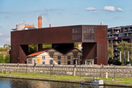 zdjęcie budynku na brzegu rzeki, dawny budynek połączony z nową architekturą, zbudowaną z metalu w rdzawym kolorze