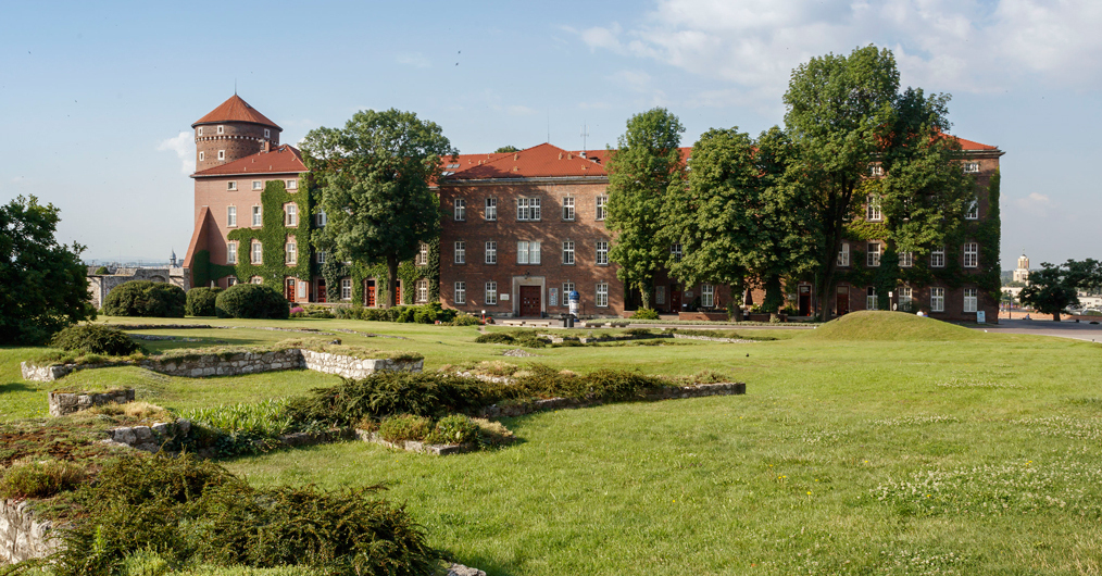 Wysoki budynek z cegły, otoczony zieloną trawą i drzewami