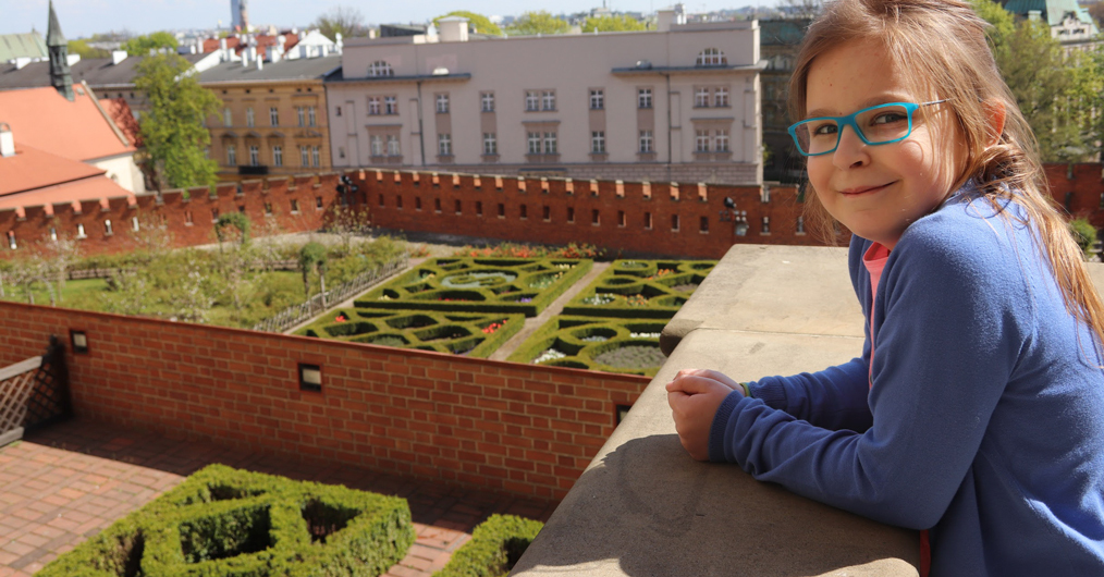widok na ogrody wawelskie, w tle budynki, z prawej strony uśmiehcnięta dziewczynka