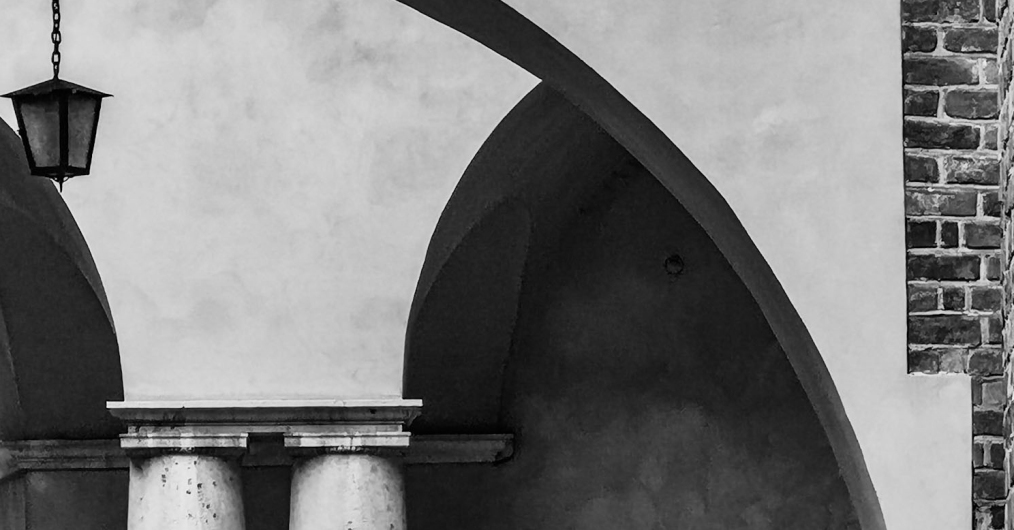 czrno-białe zdjęcie przedstawia fragment architektury: ściana z łukiem arkady a w tle druga arkada i fragmenty dwóch kolumn
