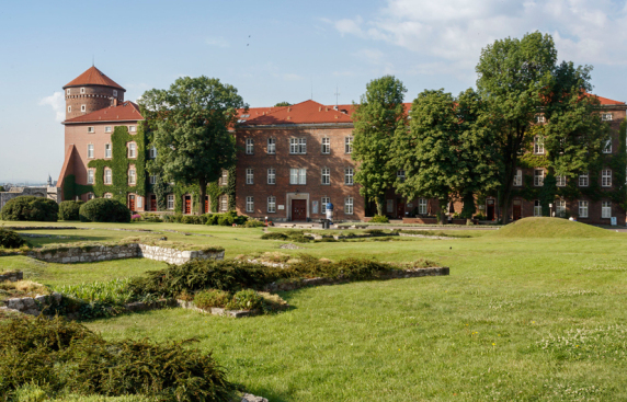 Wysoki budynek z cegły, otoczony zieloną trawą i drzewami