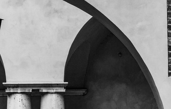 czrno-białe zdjęcie przedstawia fragment architektury: ściana z łukiem arkady a w tle druga arkada i fragmenty dwóch kolumn