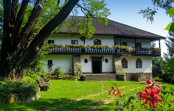 widok zabytkowego dworu, okolony balkonem, jasne tynkowane ściany, spadzisty drewniany dach,